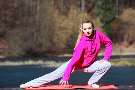 身穿粉色运动服的年轻少女在户外码头的垫子上做晨锻图片