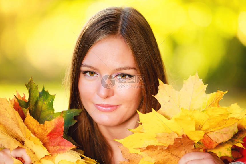 秋天季节快乐的年轻女孩肖像在秋天公园森林里拿着丰富多彩的叶子图片