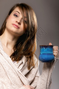 一位美丽深思熟虑的悲伤女人近身拿着一小杯温暖饮料灰色背景的蓝杯图片