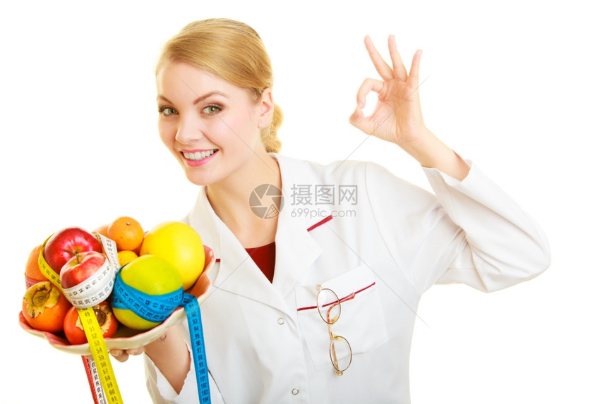 白大衣上的女人拿着水果和多彩度量的磁带被隔离医生建议健康食品显示好的手势饮食图片