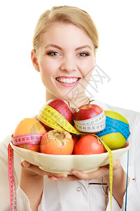 白大衣上的女人拿着水果和多彩度量的磁带被隔离图片