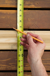 使用铅笔和胶带测量户外木甲板新雪松间空的垂直手相照片图片