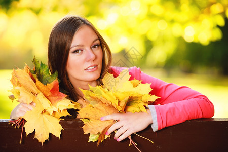 秋天季节快乐的年轻女孩肖像坐在秋天公园林的长椅上坐在图片