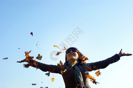 快乐的女人孩扔叶子在阳光明媚的秋天图片