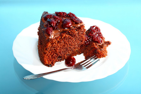 一块巧克力蛋糕有冰和樱桃白色盘子上的樱桃蓝色背景图片