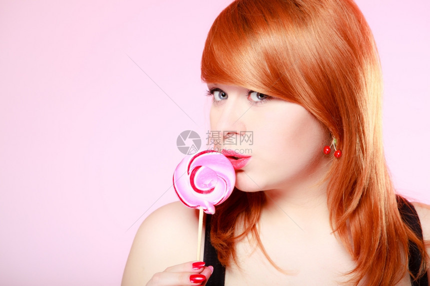 拿着糖果的感年轻女人红头发孩在粉色上吃甜的棒糖演播室拍的甜图片