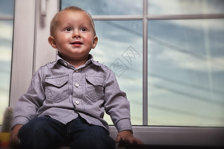 快乐的小金发男孩坐在室内窗户上图片