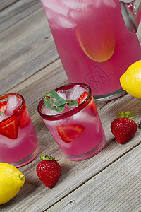 垂直角前方玻璃的垂直角视图玻璃上装满新鲜制成的粉红柠檬上面装满全柠檬草莓和半投在生锈木上的背景图片