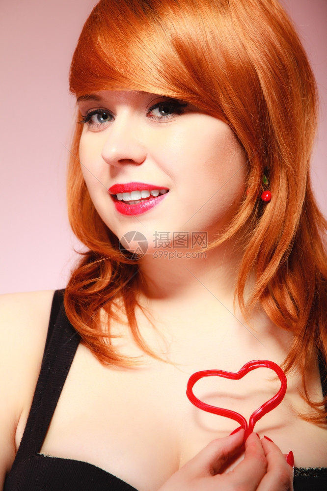 快乐和爱的概念红发女人快乐微笑的女孩胸前抱着情人节的红心图片