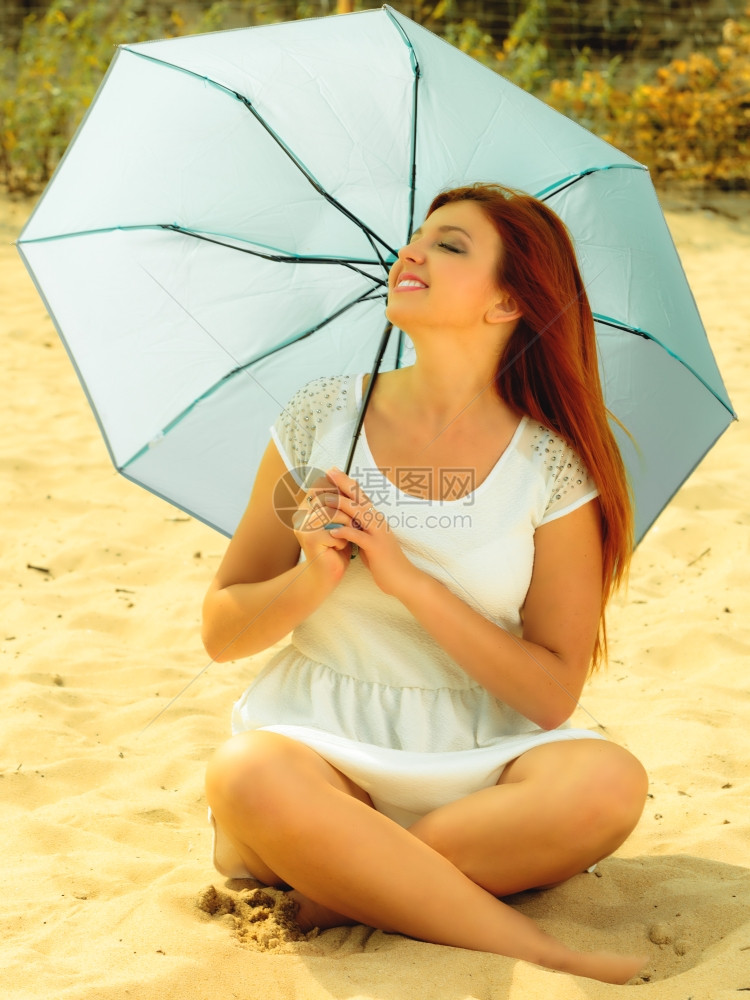 假期旅行和自由概念美丽的红发快乐女孩坐在海滩的雨伞下图片