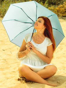 假期旅行和自由概念美丽的红发快乐女孩坐在海滩的雨伞下图片