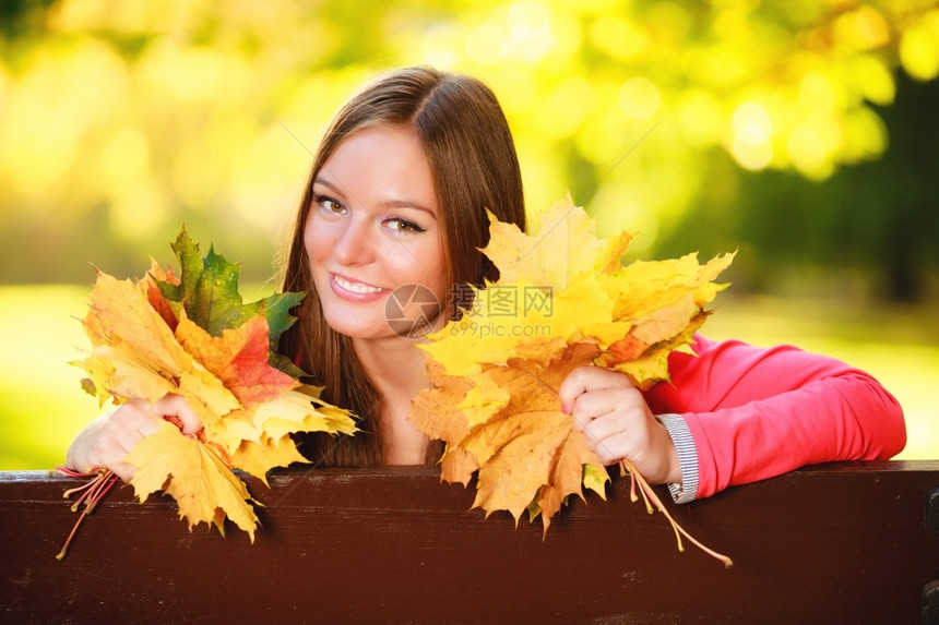 秋天季节快乐的年轻女孩肖像坐在秋天公园林的长椅上坐在图片