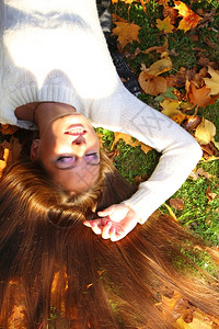 年轻女孩秋天躺落叶手下黄色的紫女孩花园背景图片