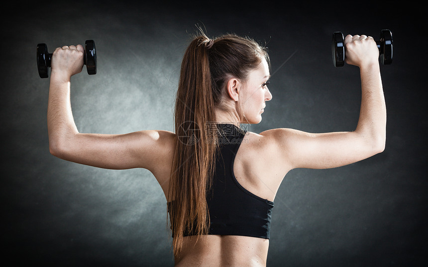 身体健康的女孩身体健康的女人举起哑铃的重量做运动用哑铃锻炼训练肩部肌肉反视灰色背景图片