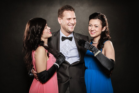 两个女人和一穿着优雅衣服的男人肖像笑着在黑色上玩耍豪华派对图片