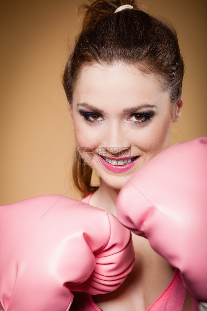 运动女拳击模特身着大有趣的粉红手套玩运动拳击演播室射棕色背景图片