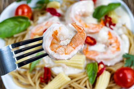 阿雷帕斯持有单虾的不锈钢叉宏观景阿尔弗雷多帕斯塔晚宴放在白盘上背景的背景