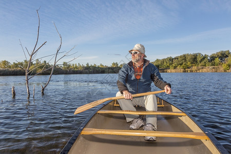 拉多涅日斯基在湖边的独木舟中享受晨日的高级牧羊人科罗拉多州林斯堡河滨池塘自然区背景