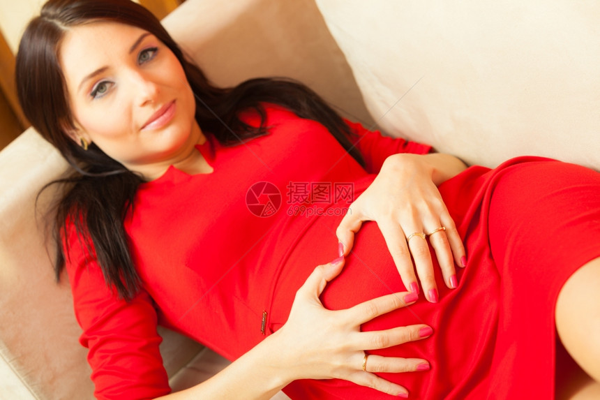 美丽的时装优雅孕妇穿着红礼服在沙发上放松图片