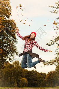 女人在秋天公园里放松跳把树叶扔在空中图片