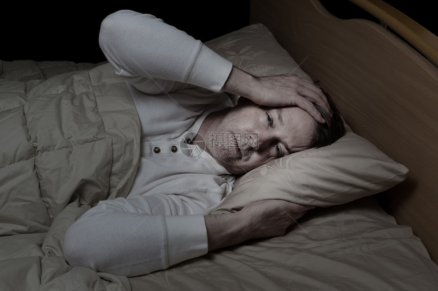 水平形象生病的成年男子抱着头在床上图片