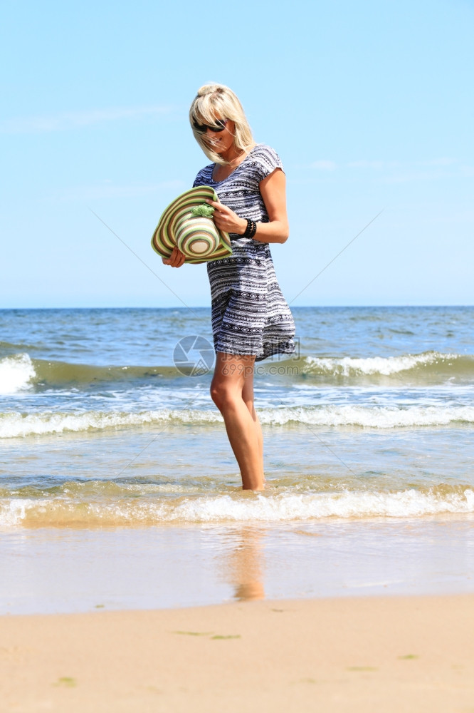 在海滩戴帽子享受暑假的全长成年女子图片