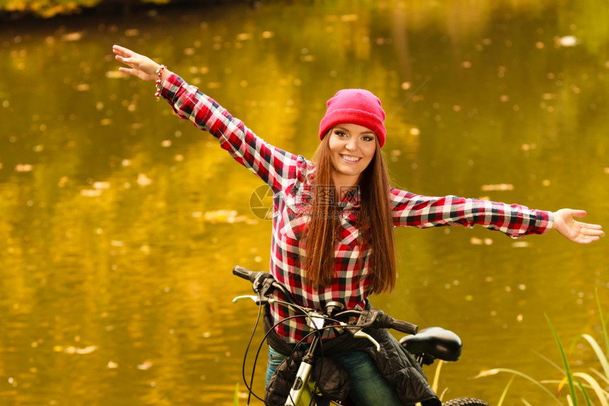 女青年公园水潭边骑着自行车舒展双臂图片