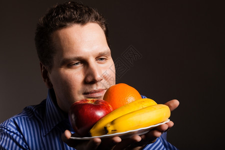 快乐的年轻人在黑暗灰色上闻到水果喜欢健康营养的人图片