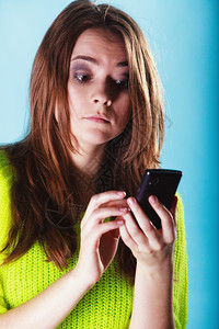 令人惊讶的少女孩在手机上发短信使用智能手机在蓝色上读写短语背景图片
