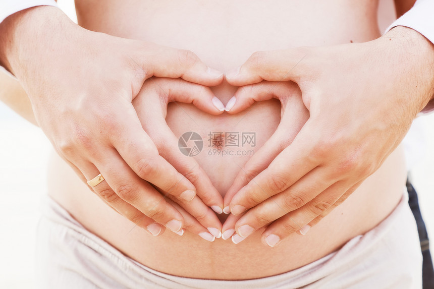 一对夫妇用双手在怀孕的肚子上做心脏形状图片