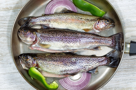 烤锅中新鲜野生鳟鱼的顶端景色洋葱和绿胡椒在生锈的白木上图片