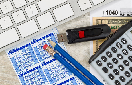 美国税表104计算器日历货币计算机拇指驱动器和木制桌面上的铅笔图片