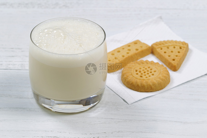 近距离地拍下一杯新鲜的牛奶在白木桌的背面上加饼干放在玻璃前唇上图片