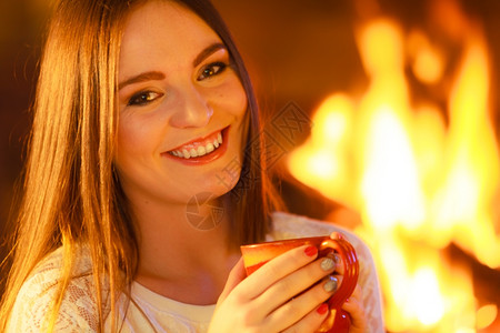 在家过冬暖气近身女人笑的长发女孩在壁炉里暖和拿着杯子喝热水图片