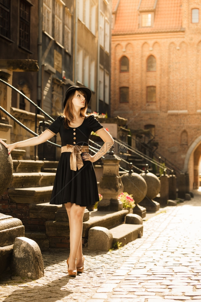穿黑帽子和着衣的回春时装女孩在旧城欧洲市GdanskDanzigPoland街上图片