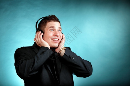 年轻快乐男子学生带耳机听音乐蓝背景的年轻快乐男子学生图片