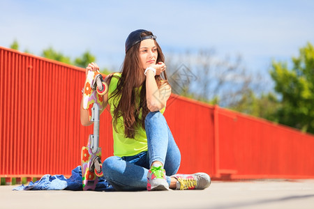 酷的十几岁女孩滑冰板坐在街上外面背景图片