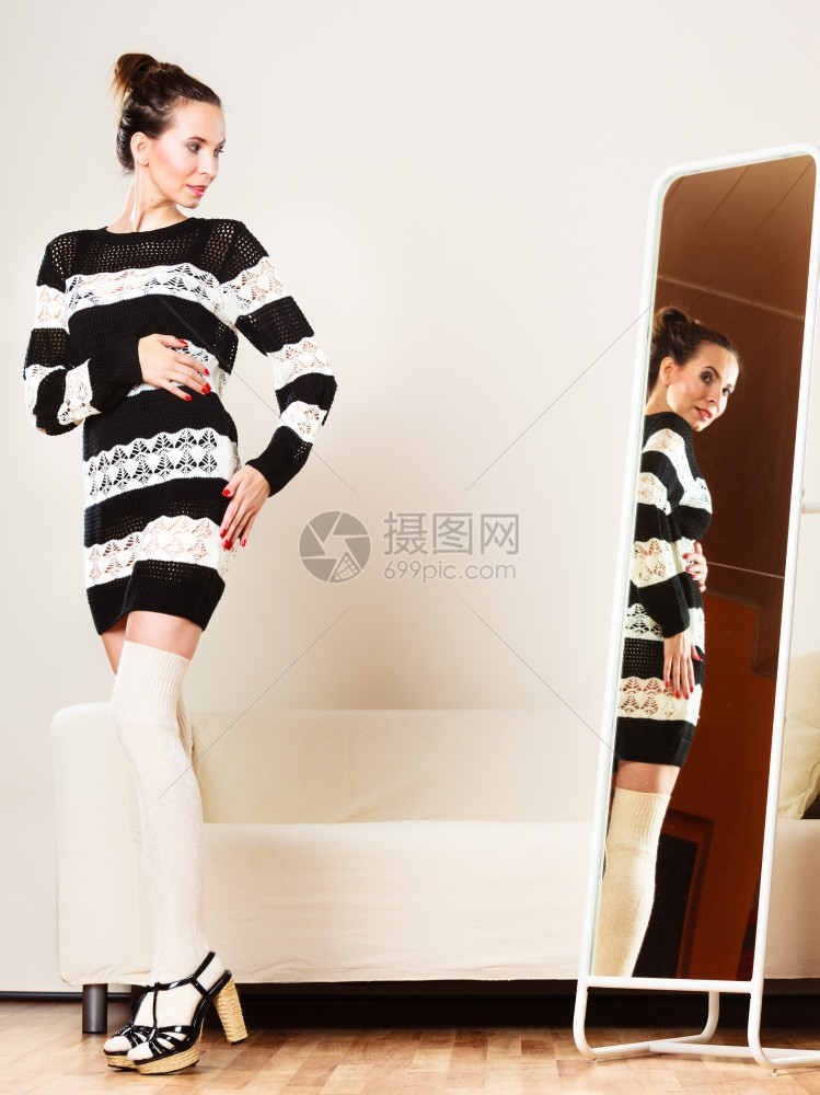 时装和购物穿着毛衣的女人选择服迷的女沙子看着镜站在服装店里图片