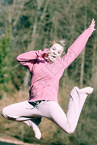 穿着粉红色运动服的年轻女孩在户外跳高健康活跃的生方式背景图片