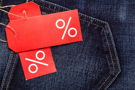 购买和销售概念关闭两个红标签在海军蓝牛仔裤口袋的棉材背景上加百分之签名和复制空间背景图片