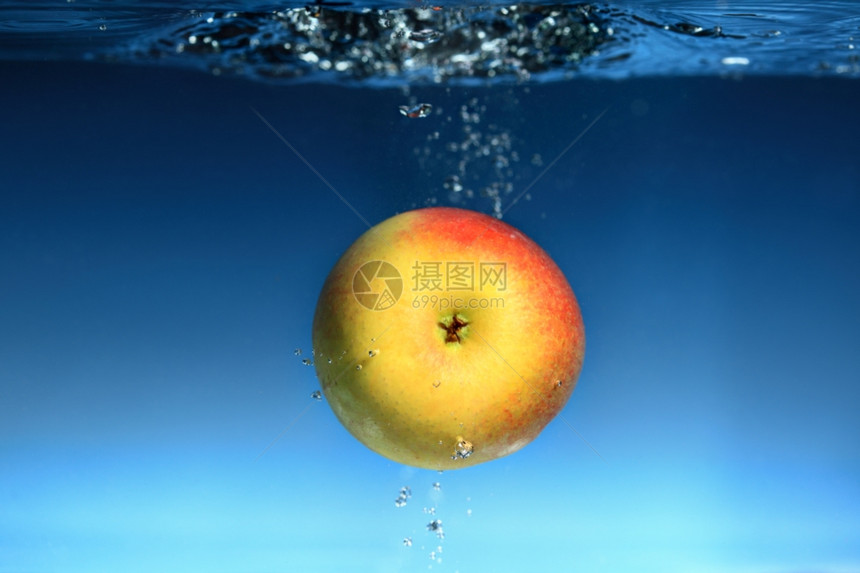 黄色红苹果在水中喷洒蓝色背景上健康的食物和活生图片