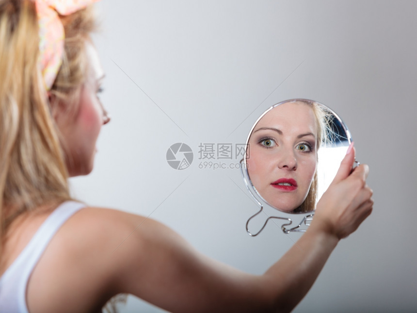 穿着发带的金美女时装郎看着镜子的倒影时装摄棚拍的灰色背景图片