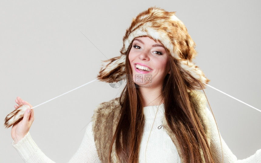 冬时的风情快乐年轻女子穿着时的冬衣毛皮帽工作室拍摄的灰色背景图片
