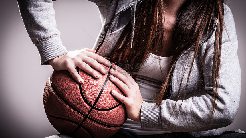 年轻运动女青长头发在灰色背景上打篮球图片