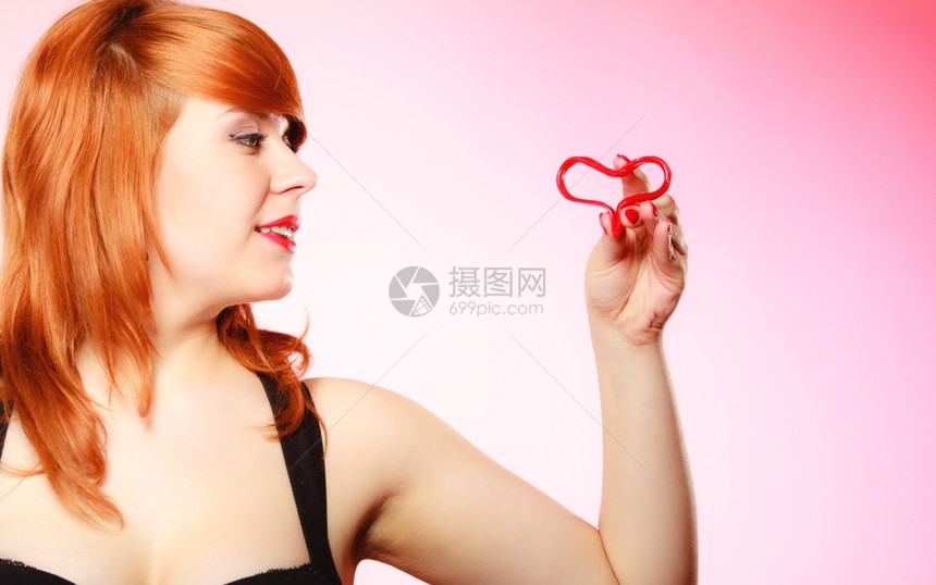 快乐和爱的概念红头发女人快乐微笑的女孩将情人红心放在粉色上情人节图片
