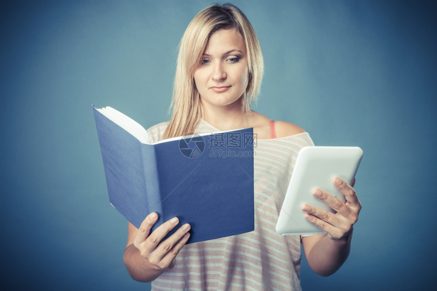 Ebookvsbook年轻女使用平板电脑阅读有传统书籍和电子阅读器的女触摸板Pc蓝背景图片