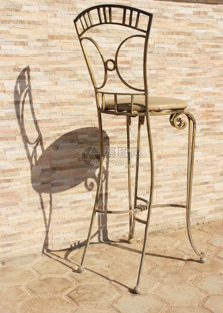 太阳光下的金属椅子旧石头背景的椅子反转投影图片