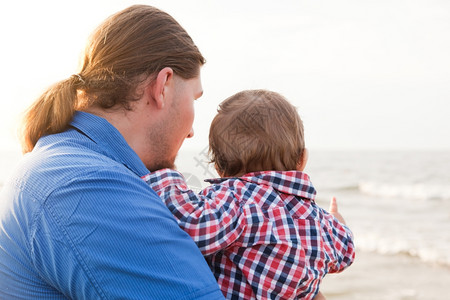 年轻父亲在海滩上抱着孩子玩得开心儿和父母的亲情图片