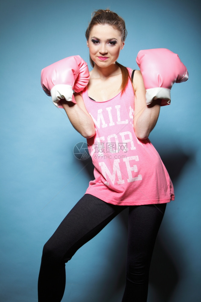 女拳击模特穿着大有趣的粉红手套玩运动拳打工作室蓝背景图片