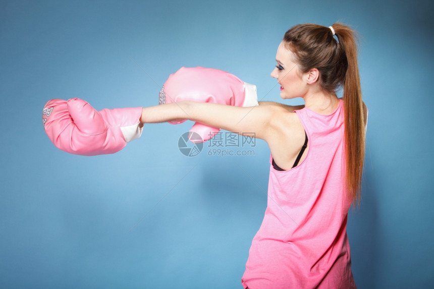 女拳击模特穿着大有趣的粉红手套玩运动拳打工作室蓝背景图片